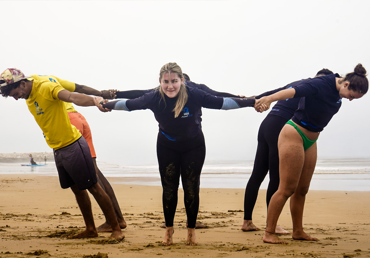 Group of guests doing fun warm-up exercises on the beach in Taghazout, Morocco. Surf preparation and team energy