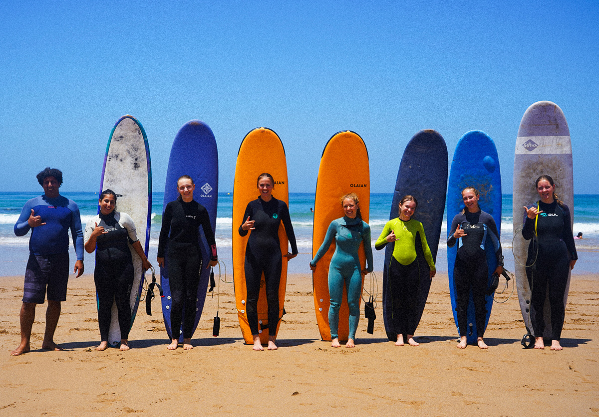 Group of guests posing with surf instructor Jalal at Nomad Surf Camp Morocco, ready for a day of surfing in Tamraght