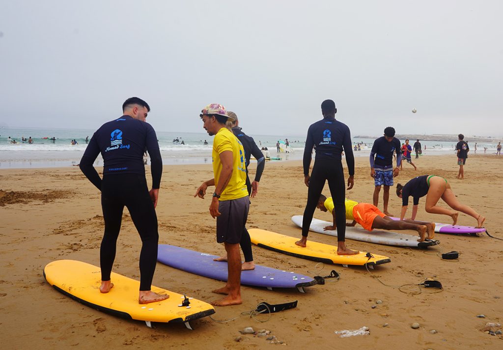 Surf instructors at Banana Beach, Tamraght, teaching guests how to stand up on their surfboards at Nomad Surf Camp Morocco.