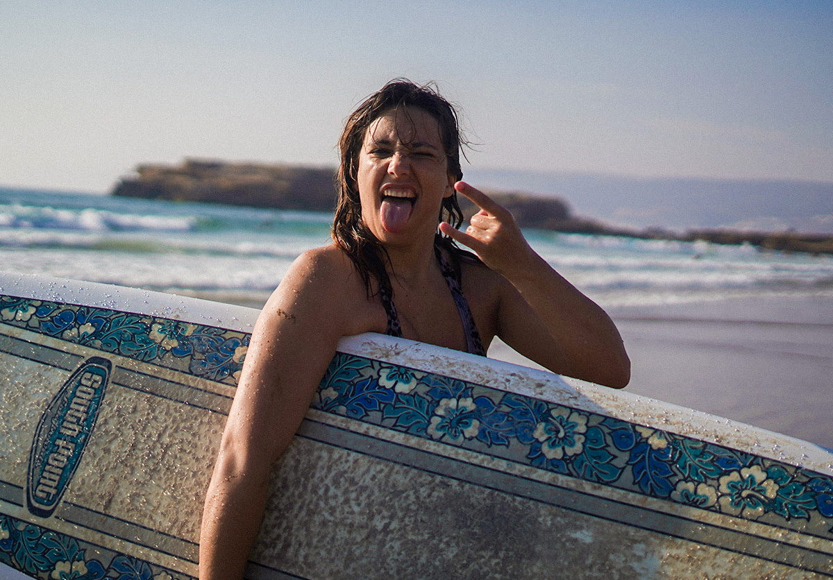 guest holding her surfboard at Devil’s Rock, Tamraght, Morocco, after catching her first wave. Surf lesson success at Nomad Surf Camp