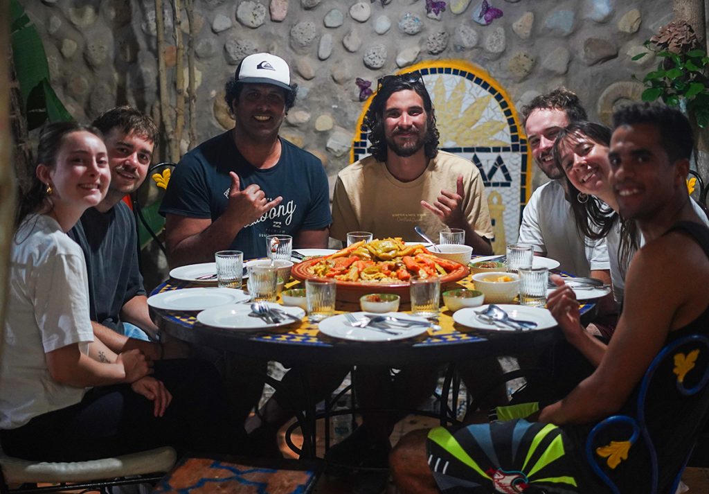 Group of surf camp guests enjoying traditional Moroccan couscous with leben at Nomad Surf Camp. Cultural dining experience in Morocco