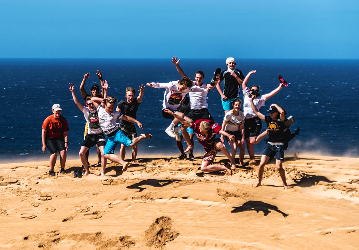 Group of people jumping on Imousouane beach after sandboarding. Fun and adventure at a Moroccan surf camp