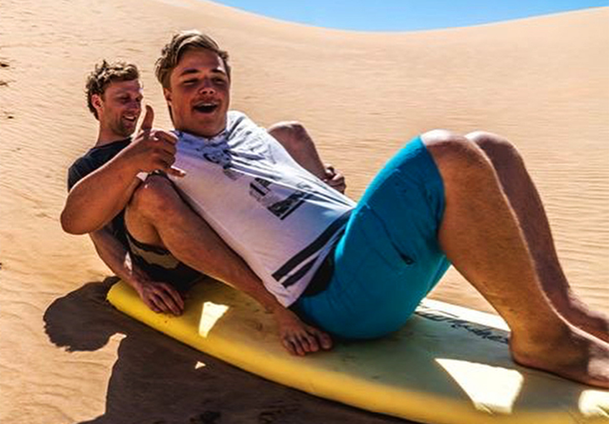 Two people trying to stay on a surfboard while sandboarding in Imousouane, Morocco.