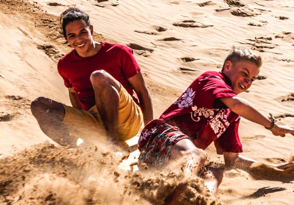 Two men laughing and riding the sand dunes in Imousouane, Morocco, enjoying an adventurous day.