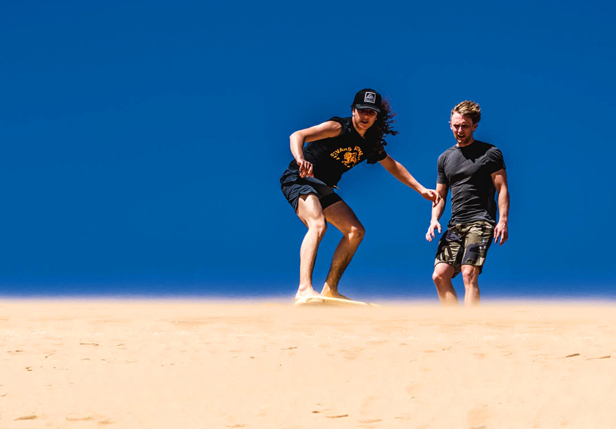 Two Nomad Surf Camp guests enjoying sandboarding on the dunes of Tamri, Morocco